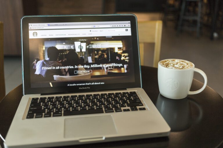 A Laptop Is Sitting On A Table Next To A Cup Of Coffee.