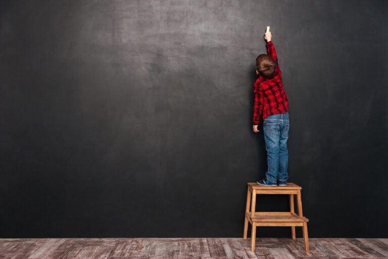 A Boy Standing On A Stool In Front Of A Blackboard.